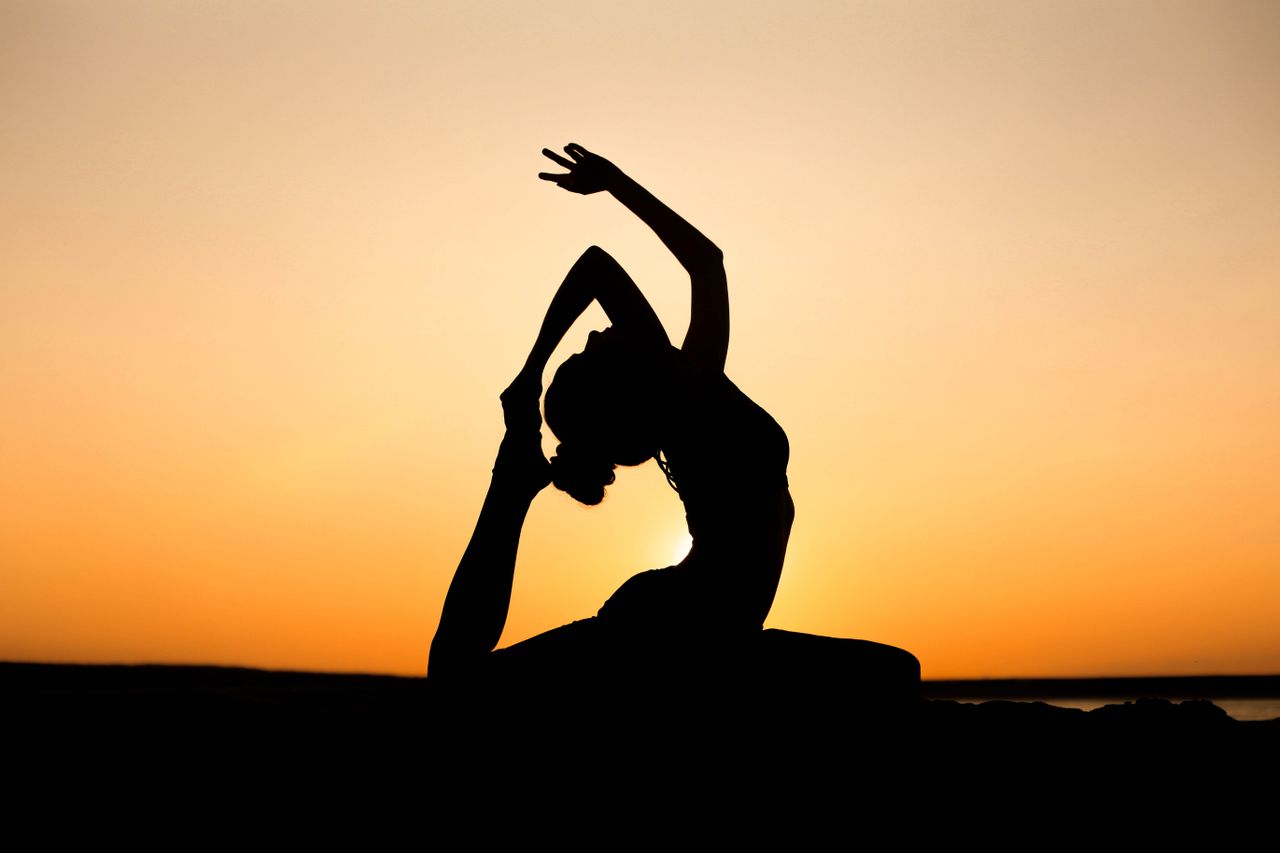 A woman in a yoga pose silhouetted against a vibrant sunset sky, embodying peace and wellness.